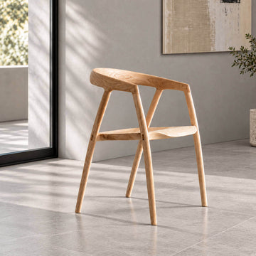 Bata solid ash wood dining chair in natural finish, featuring a sculpted curved backrest and contoured wooden seat in a minimalist grey interior.