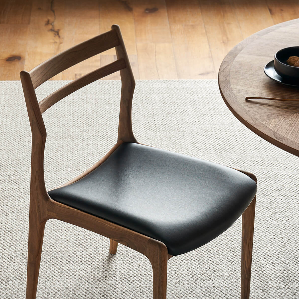 Beck solid walnut dining chair with black top grain leather seat beside round timber dining table
