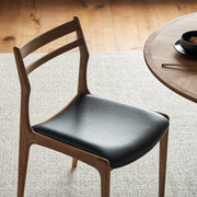 Beck solid walnut dining chair with black top grain leather seat beside round timber dining table