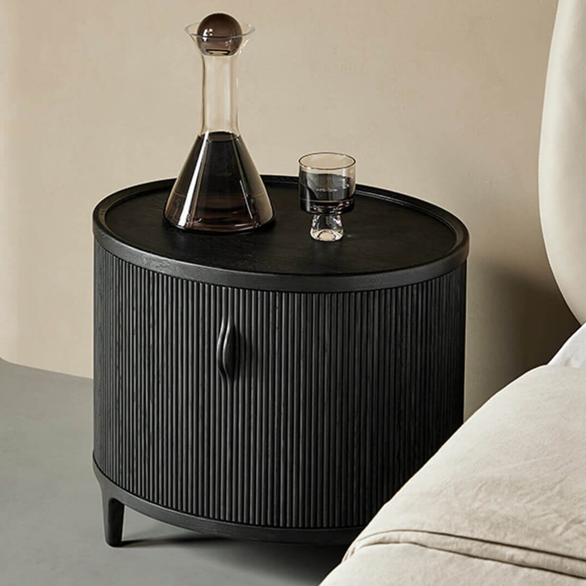Charlie Tambour Bedside Table in Black beside a bed