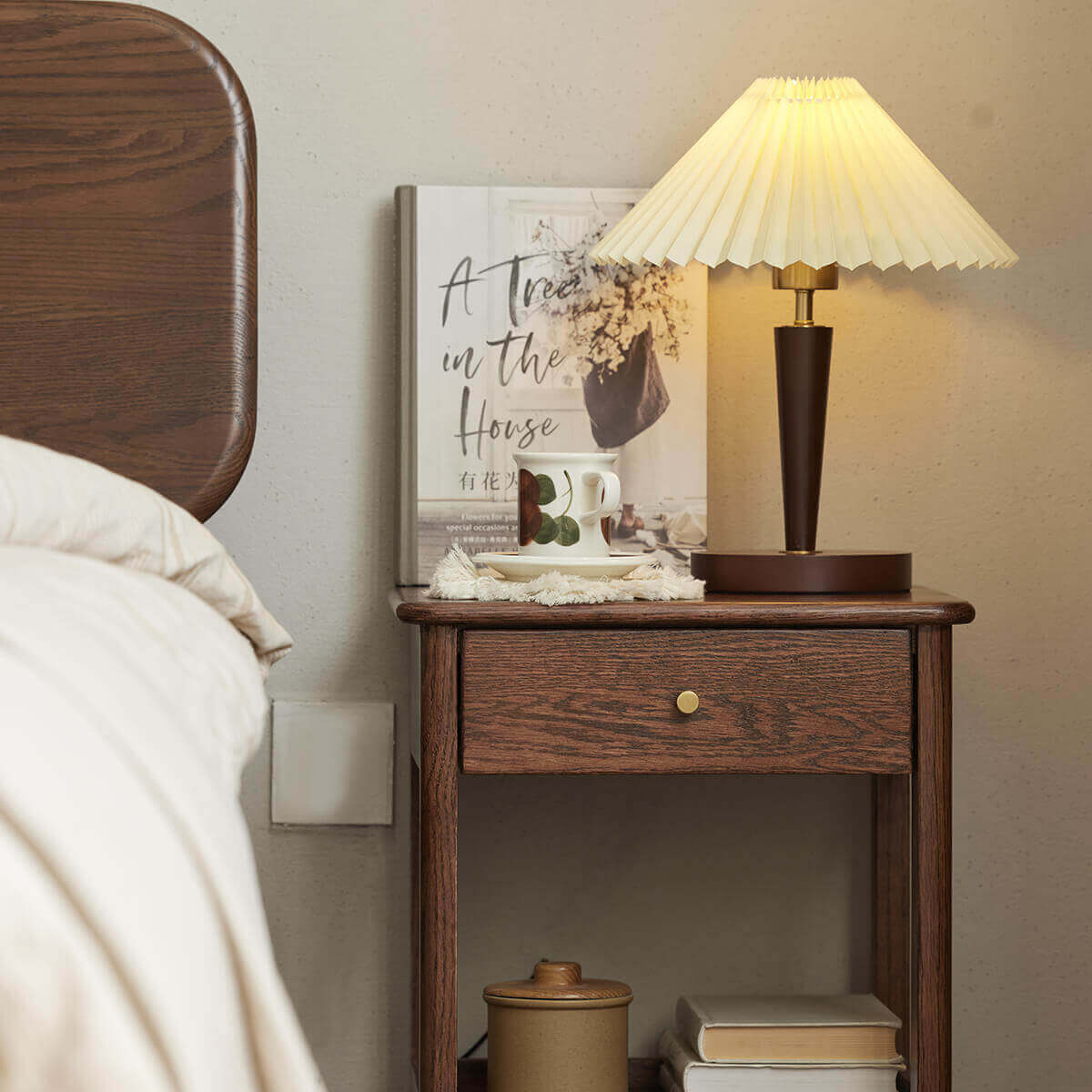 Gamo bedside table in walnut stained finish beside a bed