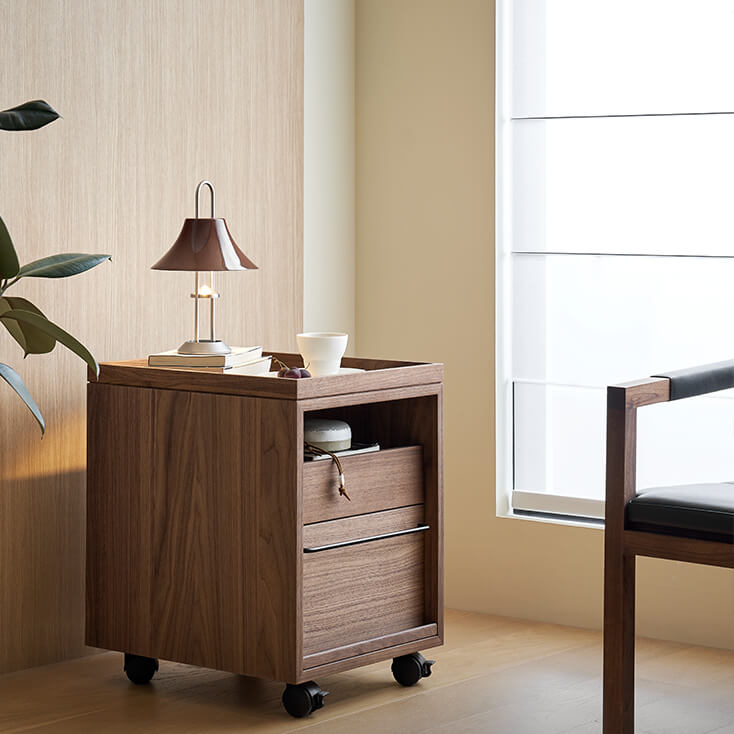 Glenn walnut storage pedestal beside a lounge chair in a modern bedroom