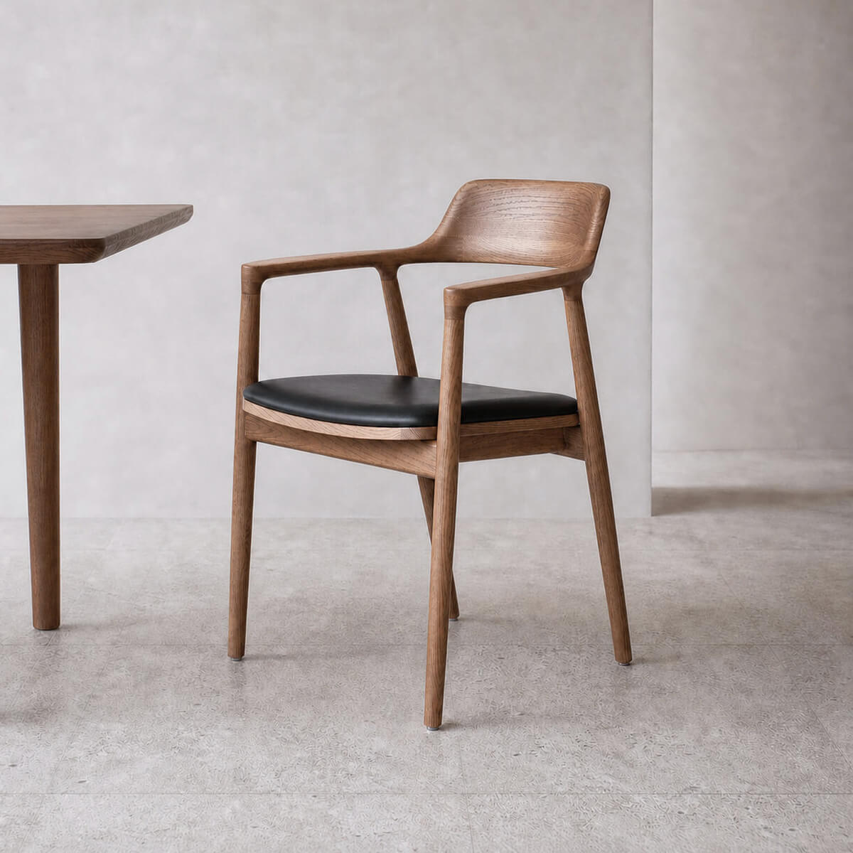 Hiroshima solid ash wood dining chair with curved wooden backrest, sculpted armrests and black leather seat in a minimalist dining setting.