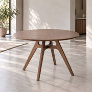 Jacob solid American ash round dining table in walnut stained finish, featuring a sculptural angled-leg base in a minimalist contemporary dining room.