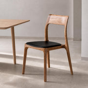 Visby Solid Ash Dining Chair in a modern dining room with natural ash wood grain and black upholstered seat